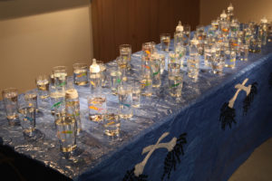 A long table with glasses set on it each containing a brighly colored beaded figure.