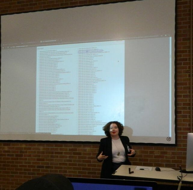 A person with curly hair standing in front of a projection of a database mid sentence.